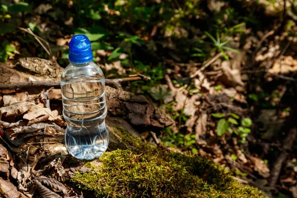 Botella de plástico con agua potable fresca sobre fondo verde del bosque — Foto de Stock