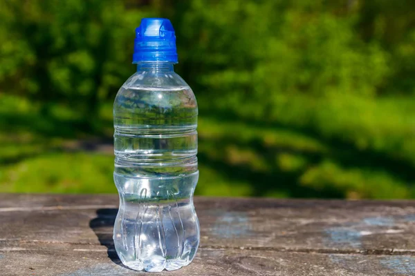 Botella de plástico con agua potable fresca sobre una mesa de madera sobre fondo natural — Foto de Stock