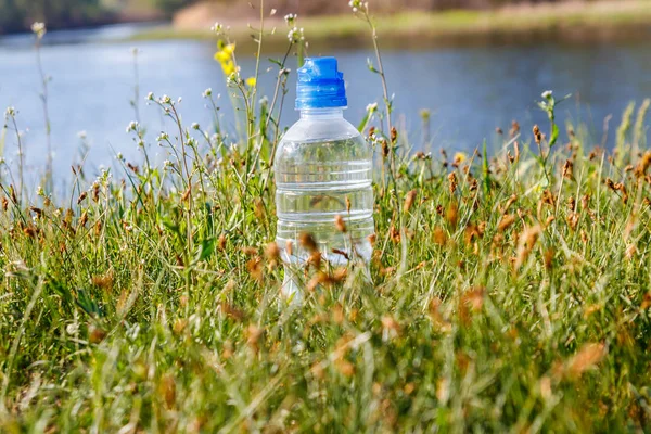 Botella de plástico con agua potable fresca en hierba verde en una orilla del río — Foto de Stock