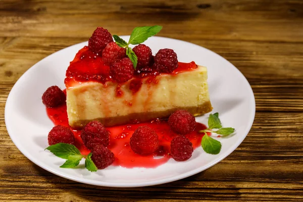 Sabroso pastel de queso de Nueva York con frambuesas y mermelada de frambuesa en un plato blanco sobre una mesa de madera — Foto de Stock