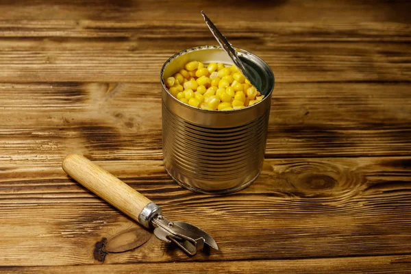 Open tin can of corn and can opener on wooden table — Stock Photo, Image