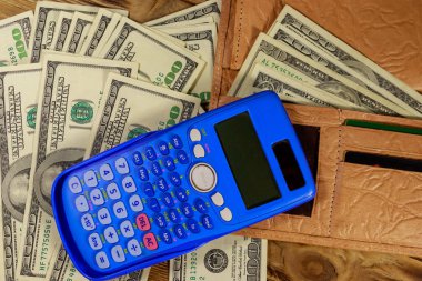 Açılan cüzdan, hesap makinesi ve ahşap masa üzerinde Amerikan doları banknotlar. Üstte görüntü