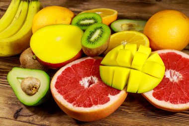 Ahşap masa üzerinde tropikal meyve çeşitleri. Muz, mango, portakal, avokado, greyfurt ve kivi ile natürmort
