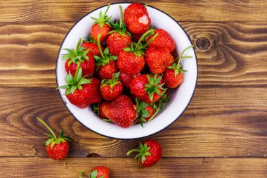 Tahta bir masada beyaz kasede taze olgun çilek. Üst görünüm