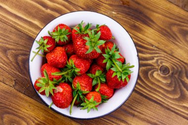 Tahta bir masada beyaz kasede taze olgun çilek. Üst görünüm