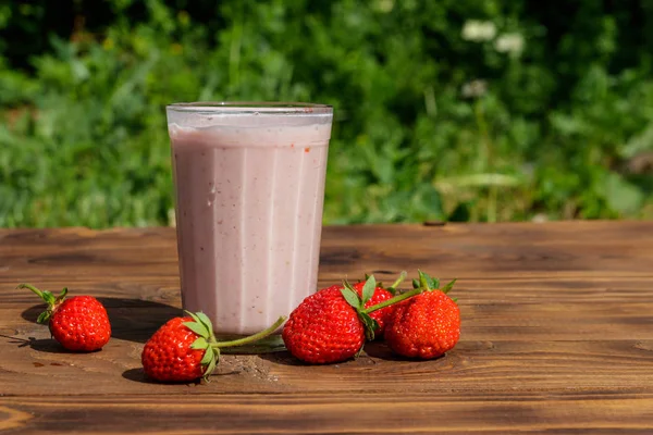 Dışarıdaki ahşap masada bir bardak taze çilekli smoothie. 