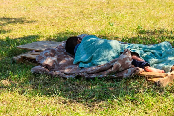 Бездомный мальчик спит на траве в городском парке. Концепция бедности — стоковое фото