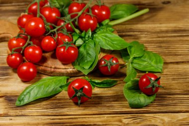 Tahta bir masada yeşil fesleğen yapraklı taze kiraz domatesleri.