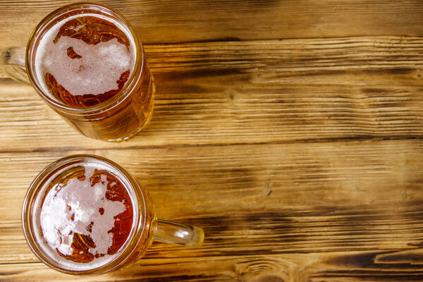 Two mugs of beer on a wooden table. Top view, copy space