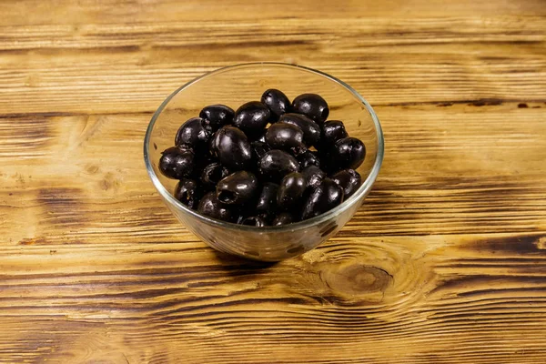 Olive nere sottaceto in ciotola di vetro sul tavolo di legno — Foto Stock