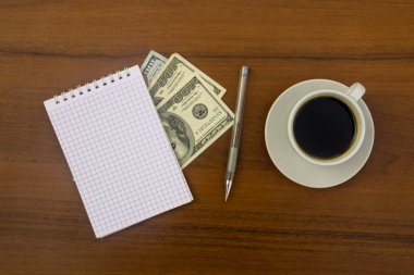 Fincan kahve, dolar, not defteri ve kalem ahşap masa