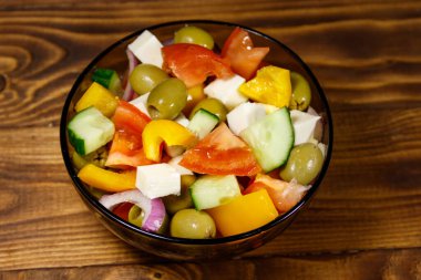 Taze sebze ile Yunan salatası, beyaz peynir ve yeşil zeytin cam ahşap masaya kase.