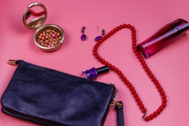 Debriyaj çantası, kırmızı kolye, küpeler, oje, ruj topları ve pembe arka planda bir şişe parfüm. Güzellik ve moda konsepti. Düz yatıyordu