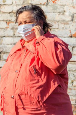 Kıdemli kadın yüzünde Coronavirus ve diğer virüs ve hastalıklara karşı koruyan tıbbi bir maske takıyor. Eski tuğla duvarın arka planında. Koronavirüs salgını