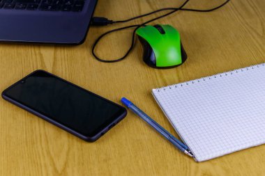 Bilgisayarda fare, akıllı telefon, defter ve kalem var. Ev ve iş konseptinde çalışmak