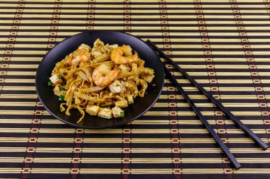 Tayland usulü kızarmış pirinç eriştesi, karides ve bambu hasırında soya peyniri. Tayland yemeği.