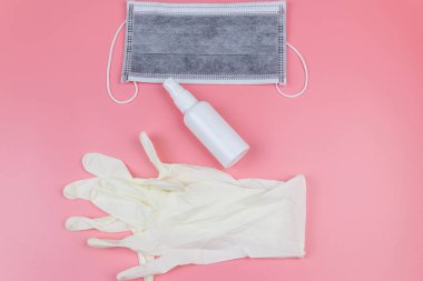 Koruyucu tek kullanımlık tıbbi maske, eldivenler ve pembe arka planda el dezenfektanı. Üst görünüm