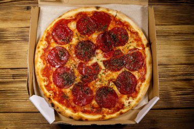 Tahta bir masanın üzerindeki karton kutuda nefis taze pizza. Üst Manzara. Yemek teslimatı, fast food, pizza teslimatı.