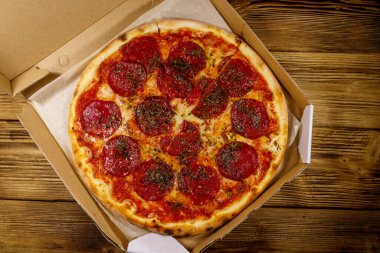 Tahta bir masanın üzerindeki karton kutuda nefis taze pizza. Üst Manzara. Yemek teslimatı, fast food, pizza teslimatı.