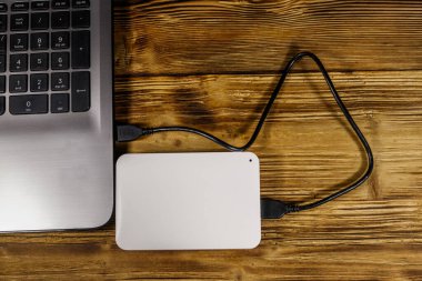 Harici HDD, tahta bir masadaki dizüstü bilgisayara bağlı. Üst Manzara. Veri depolama kavramı