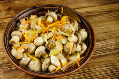 Tahta masadaki seramik kasede havuç, soğan ve baharatla marine edilmiş lezzetli mantarlar.