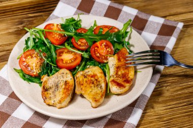 Kızarmış tavuk göğsü, taze roka salatası ve ahşap masada vişneli domates.