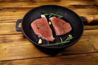 Biberiye, sarımsak ve baharatlı çiğ domuz bifteği ahşap masada ızgara demir tavada pişirilmeye hazır.