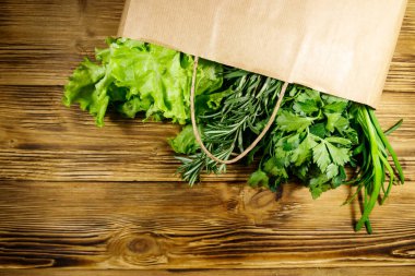 Yeşil soğanlı kağıt torbası, biberiye, marul yaprakları ve ahşap masada maydanoz. Üst Manzara. Sağlıklı gıda ve market alışverişi kavramı