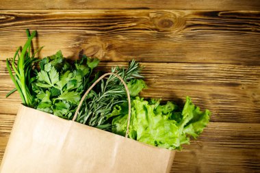 Yeşil soğanlı kağıt torbası, biberiye, marul yaprakları ve ahşap masada maydanoz. Üst Manzara. Sağlıklı gıda ve market alışverişi kavramı