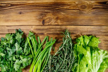 Taze maydanoz, marul yaprakları, yeşil soğan ve ahşap masada biberiye. Üst görünüm