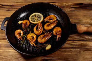 Baharatlı ızgara karides, biberiye ve limon ızgara tavada ahşap bir masada.