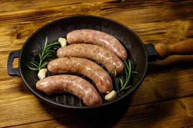 Çiğ sosisler hazır biberiye, sarımsak ve baharatlarla ahşap masada ızgara ızgara demir tavada.