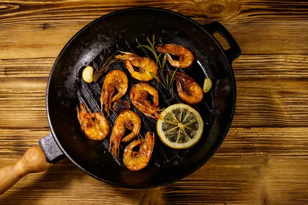 Grilled shrimp with spices, rosemary and lemon in a grill frying pan on a wooden table. Top view