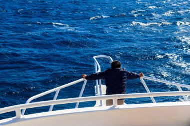 Yatın beyaz pruvasında duran ve denize ya da okyanusa bakan bir adam. Lüks tatil konsepti. Arka plan