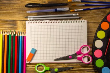 Okul Kırtasiye malzemeleri kümesi. Boş defter, kalem, kalem, suluboya boyalar, makas, Boya fırçaları, silgi ahşap masa üzerinde renkli. Geri okul kavramı