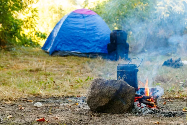 Cooking on campfire in camping. Tent and backpack on background