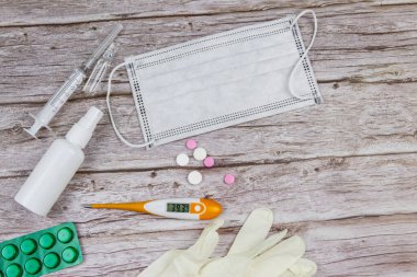 Koronavirüsü önleme ve tedavi etme kavramı. Tıbbi maske, el dezenfektanı, elektronik termometre, haplar, şırınga, ampuller, ahşap arka planda tıbbi eldivenler. Üst görünüm