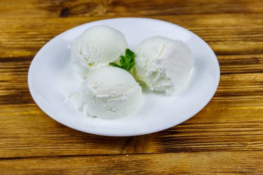 Tahta bir masada beyaz tabakta vanilyalı dondurma.