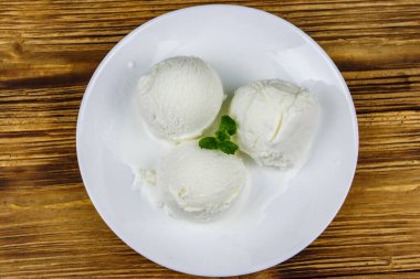 Tahta bir masada beyaz tabakta vanilyalı dondurma. Üst görünüm