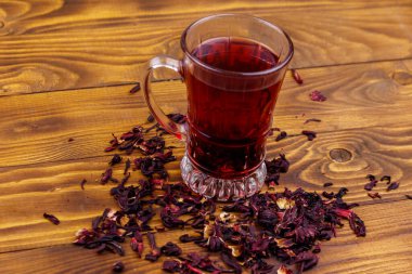 Ahşap masada bir bardak kırmızı amber çayı (carcade, roselle).