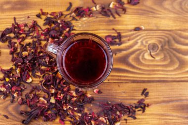 Ahşap masada bir bardak kırmızı amber çayı (carcade, roselle).