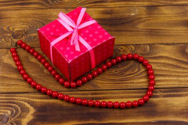 Ahşap arka plan üzerinde hediye kutusu ve kırmızı boncuk kolye