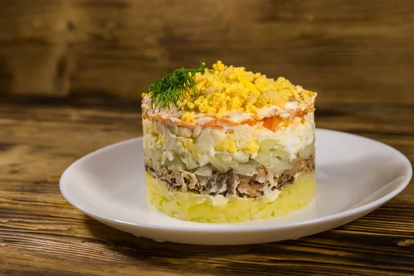 Ahşap masada geleneksel Rus salatası Mimoza. Sardalya, soğan, patates, havuç, peynir, yumurta ve mayonez ile katmanlı salata