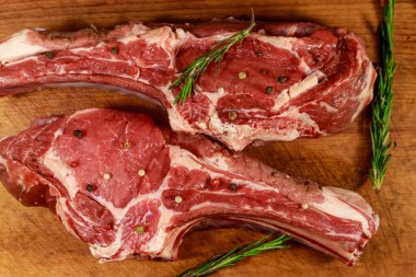 Kemiğin üzerinde çiğ biftek, baharatlar ve ahşap masada biberiye. Üst görünüm