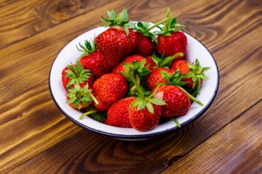 Tahta bir masada beyaz kasede taze olgun çilek.