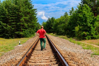 Yalnız adam tren yolunda yürüyor.