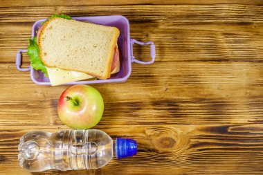 Sandviçli beslenme çantası, ahşap bir masada bir şişe su ve elma. Üst görünüm, alanı kopyala