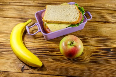 Sandviç, muz ve elmayla birlikte ahşap bir masada.