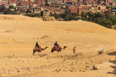 Kahire, Mısır - 8 Aralık 2018: Kahire şehir manzarasına karşı Giza platosunda deveye binen turistler