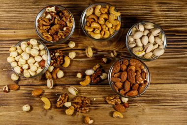 Ahşap masada fındık çeşitleri. Badem, fındık, şam fıstığı, ceviz ve cam kaselerde ceviz. Üst Manzara. Sağlıklı yeme kavramı
